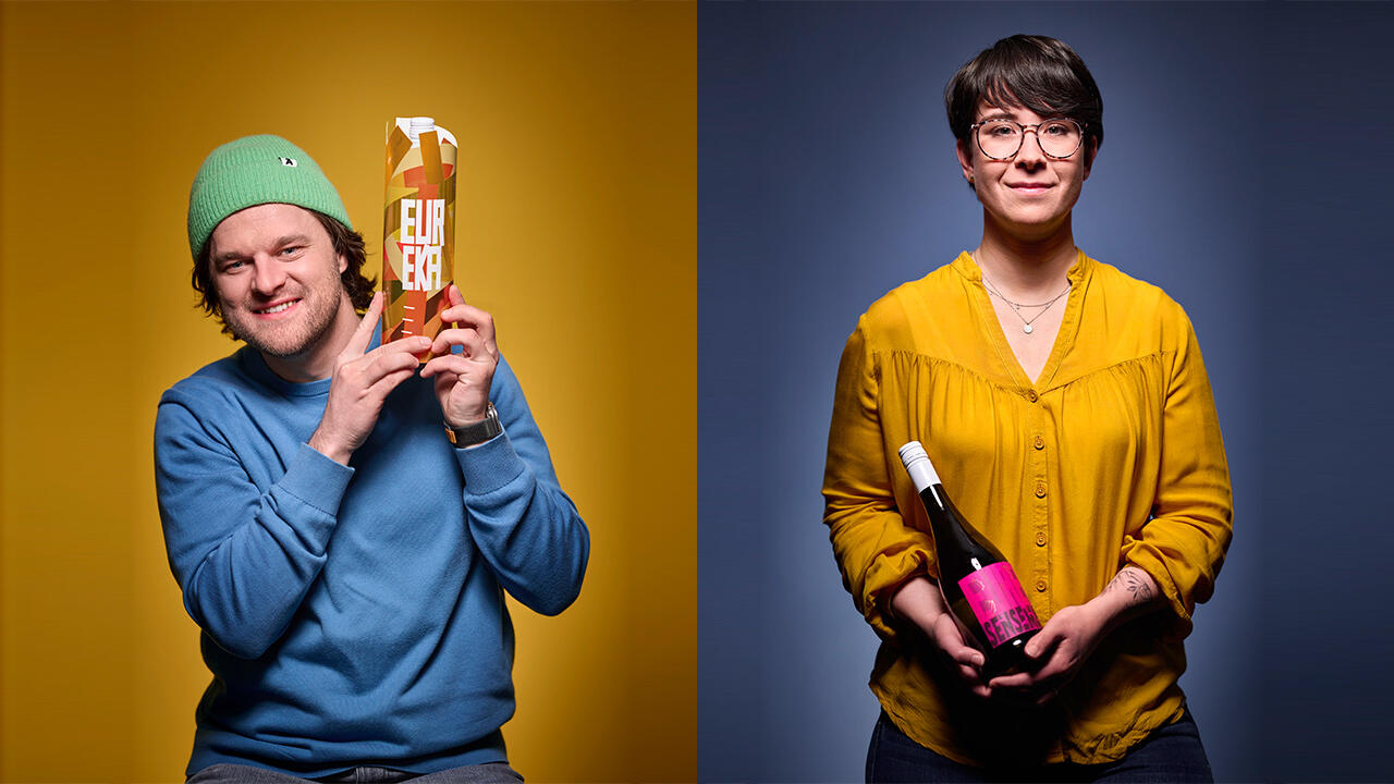 Man in blue sweater holding up a cardboard bottle pack, woman in yellow blouse holding a white wine bottle