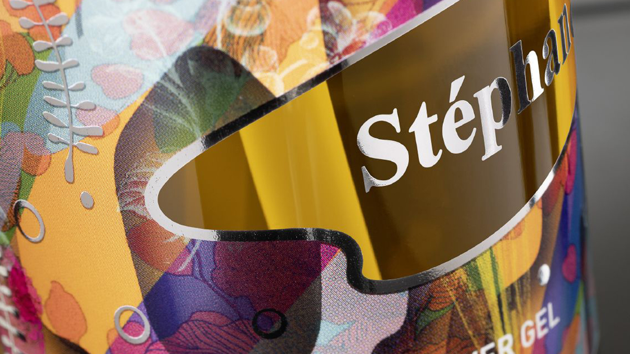 KURZ digital printing awakes customers desire Bottle close-up with digitally printed gold and silver shining elements next to floral background design