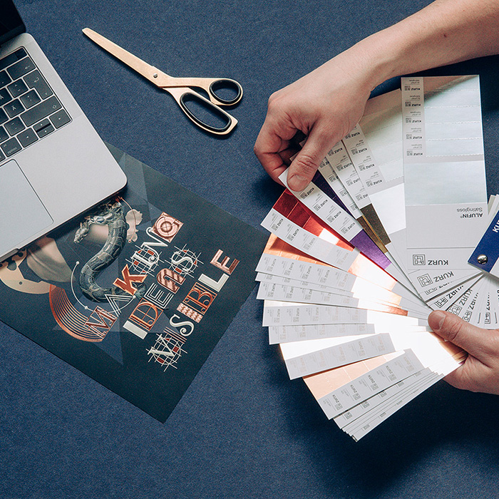 Photo with office supplies and hands searching through a sample book with shiny finishes